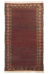 Alfombra de fondo oscuro con patrón repetitivo en tonos rojos y borde decorativo beige con detalles intrincados.
