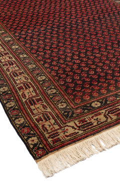 Vista en ángulo de una alfombra con un diseño repetitivo en tonos rojos sobre un fondo oscuro, bordeada por un marco beige decorativo.