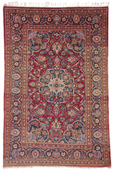 Alfombra persa clásica con un diseño floral central en tonos rojos y azules, rodeada por un borde decorativo detallado.