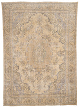Vista en ángulo de una alfombra beige antigua con intrincados diseños florales en tonos desgastados.