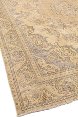 Vista completa de una alfombra beige con un diseño central floral y un borde decorado con motivos clásicos en tonos neutros.