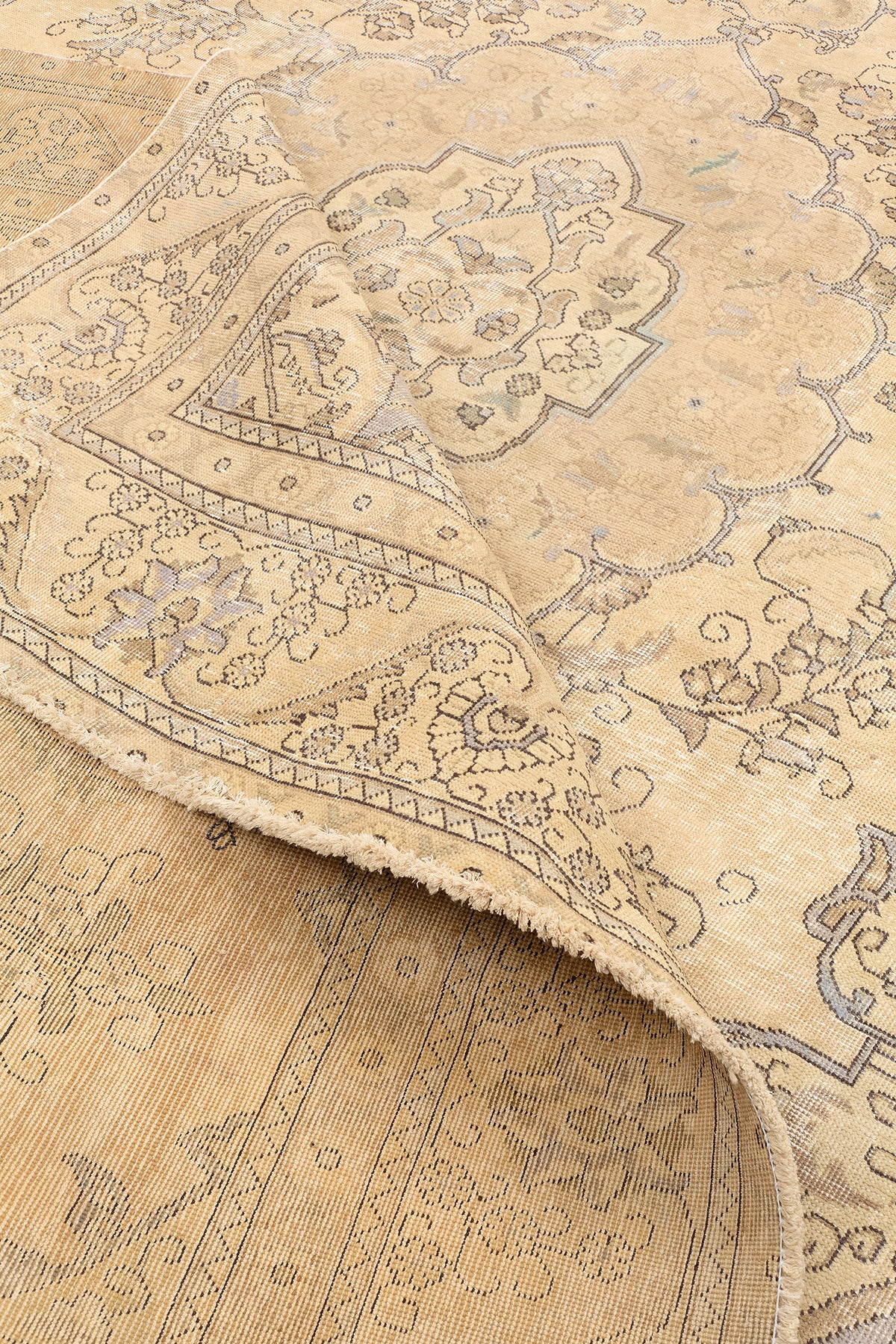 Esquina de una alfombra beige con detalles ornamentales florales y bordes ligeramente desgastados.