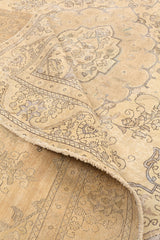 Esquina de una alfombra beige con detalles ornamentales florales y bordes ligeramente desgastados.