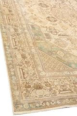 Vista lateral de la esquina de una alfombra oriental beige con detalles marrones y verdes.