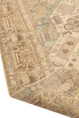 Detalle del borde enrollado de una alfombra oriental beige con patrones geométricos marrones y verdes.