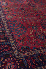 Vista cercana de los patrones de árboles y flores sobre un fondo rojo vibrante en la alfombra persa.