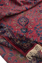 Doblado de la alfombra persa revelando la textura de los hilos y el borde trenzado con detalles florales en tonos rojos y azules.