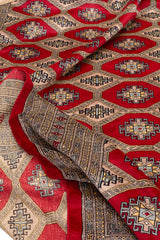 Alfombra plegada resaltando los detalles del patrón geométrico en tonos rojos y beige.