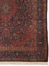Detalle del borde y centro geométrico floral de la alfombra persa con tonos rojos profundos y azul oscuro.