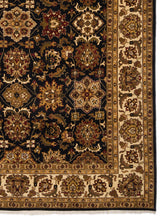 Detalle del borde de una alfombra con motivos florales en tonos marrón y beige sobre un fondo oscuro.