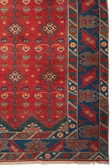 Detalle del borde azul de la alfombra con patrones geométricos en rojo y beige, mostrando la riqueza de sus colores.