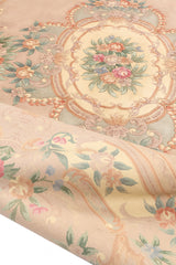Alfombra beige floral enrollada, mostrando la textura y los detalles intrincados de las flores y los bordes