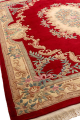 Vista en ángulo de alfombra roja con patrón floral central y borde ornamentado.