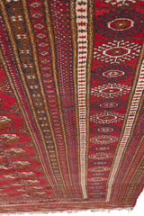 Perspectiva lateral de alfombra con patrones tribales geométricos en tonos rojos y marrones.