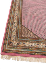Primer plano del borde de una alfombra con patrones geométricos en marrón, rosado y beige.