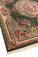 Borde de la alfombra verde enrollado mostrando el detalle floral en la trama beige y verde.