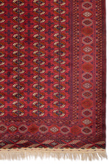 Detalle del borde superior de una alfombra oriental roja con figuras geométricas en tonos oscuros y claros.