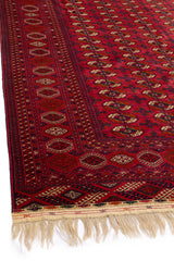 Vista en ángulo de alfombra oriental, resaltando los detalles del borde con patrones simétricos y colores cálidos.