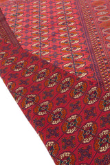 Alfombra oriental con diseño geométrico en tonos rojos, con una esquina doblada para mostrar los detalles del reverso y el patrón.