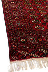 Patrón simétrico en tonos rojos y naranjas con borde decorativo en una alfombra tradicional.
