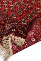 Alfombra roja enrollada con detalles geométricos en blanco, negro y tonos tierra.