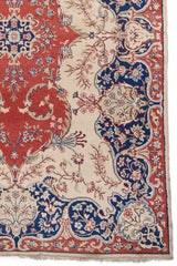 Detalle del borde de la alfombra mostrando un delicado diseño floral en tonos beige y azul sobre un fondo rojo vibrante.