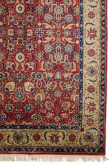 Vista en detalle del borde lateral derecho de una alfombra roja con motivos florales y un elegante marco beige.