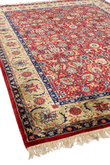 Esquina inferior derecha de una alfombra de diseño clásico en rojo, beige y azul con detalles de flores y hojas.