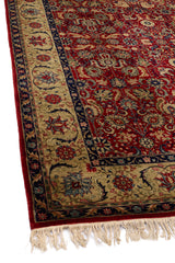 Parte lateral izquierda de una alfombra con intrincados patrones florales rojos y azules, resaltados por un borde beige con flecos.