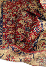  Primer plano del tejido y la parte trasera de una alfombra de motivos florales rojos con bordes decorados en beige y azul.