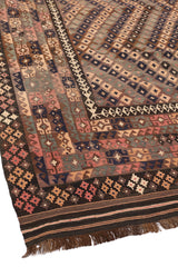Borde inferior de la alfombra tribal, con patrones geométricos simétricos en tonos oscuros y rojizos.