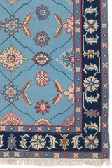 Detalle de la alfombra con diseños geométricos y florales en colores pastel sobre un fondo azul.