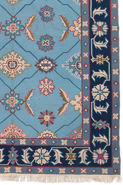 Detalle de la alfombra con diseños geométricos y florales en colores pastel sobre un fondo azul.