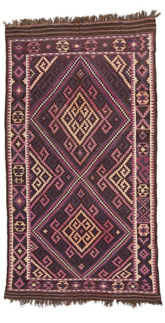 Alfombra de fondo marrón oscuro con patrones geométricos en tonos rosa, morado y beige.