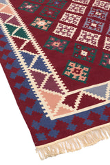 Primer plano de la alfombra kilim doblada, resaltando la textura y la combinación de colores burdeos, verdes y azules en sus bordes.