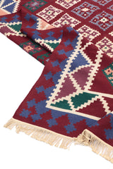 Detalle de la esquina de una alfombra kilim mostrando los flecos y los patrones geométricos triangulares en sus bordes coloridos.