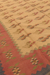 Vista cercana de los patrones geométricos de una alfombra kilim, resaltando los colores mostaza, verde y rojo.