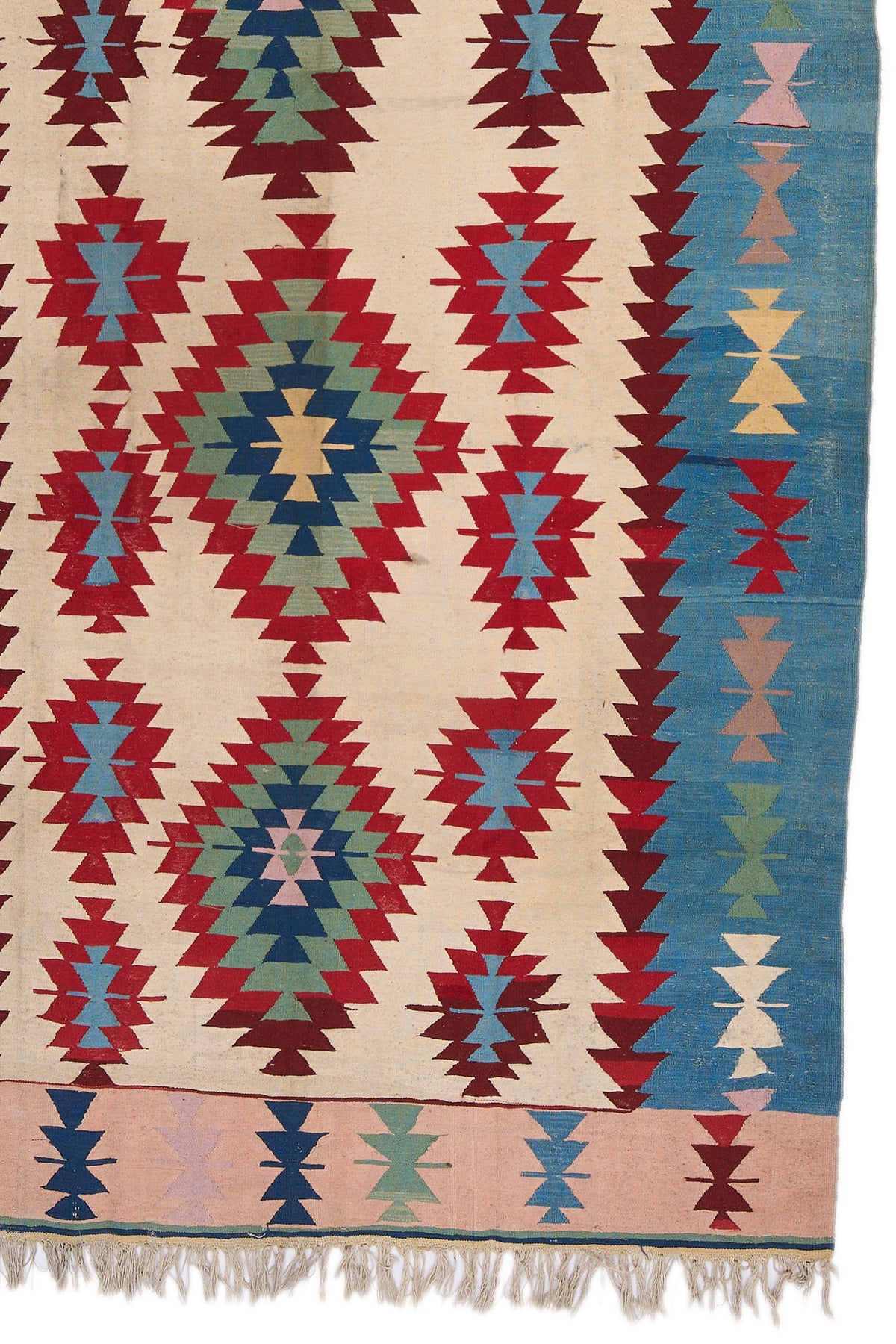 Detalle de patrón geométrico central en la alfombra kilim de tonos cálidos con bordes en beige.