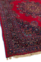 Primer plano del borde floral de la alfombra mostrando la combinación de tonos oscuros y rojos con intrincados detalles.