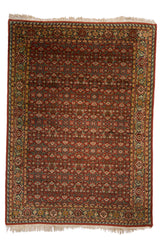 Alfombra oriental de fondo rojo con un detallado diseño floral en tonos azules y beige.