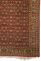 Esquina inferior de una alfombra oriental roja con detalles florales azules y beige.