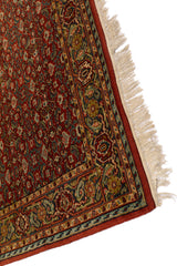 Vista en ángulo de la alfombra oriental roja resaltando su borde decorativo en azul y beige.