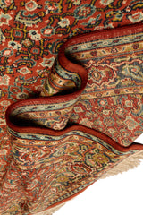 Alfombra oriental enrollada, mostrando sus bordes decorativos con patrones florales.
