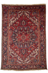 Alfombra oriental con un intrincado diseño geométrico y bordes florales en tonos rojos y azules.