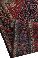 Alfombra persa con fondo rojo y bordes azul oscuro, decorada con motivos florales intrincados y patrones curvos.