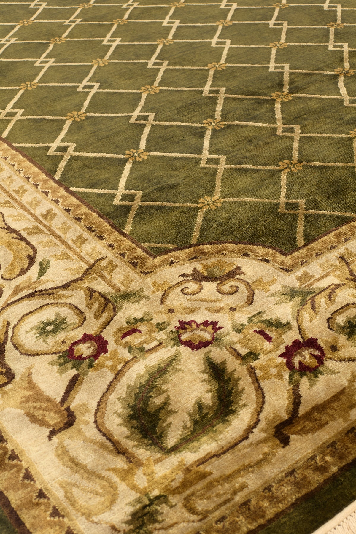 Acercamiento al borde beige de una alfombra verde con detalles florales en tonos marrones y verdes.