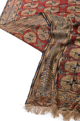 Alfombra oriental plegada, mostrando tanto el patrón geométrico en rojo, beige y azul, como el reverso textil.