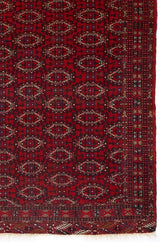 Detalle del patrón geométrico en una alfombra roja con borde intrincado y diseño repetitivo.