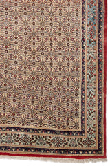 Primer plano de la esquina de una alfombra octagonal con bordes florales en tonos rojos y beige.