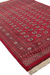 Alfombra persa con patrones geométricos repetitivos y bordes rojos y azules.